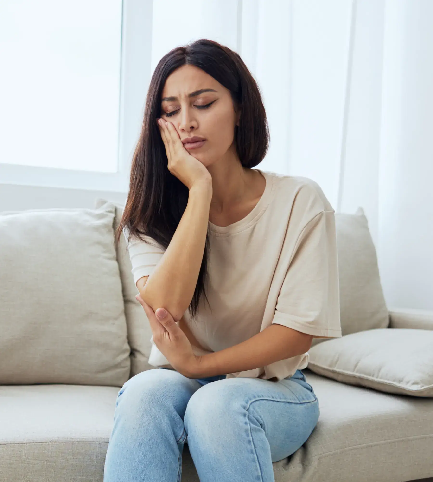 A woman sitting on a couch holding her hand to her face.
