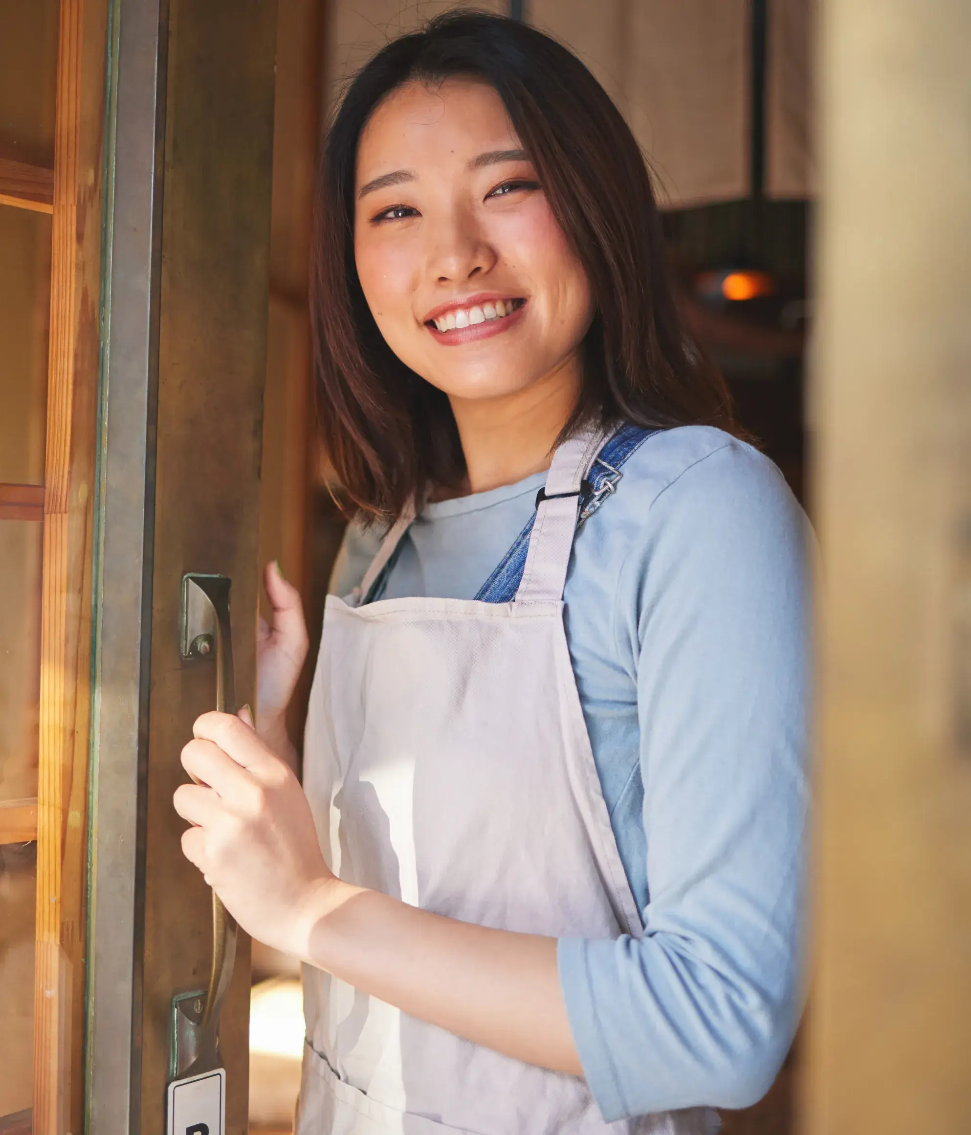 A woman in an apron holding a door handle.